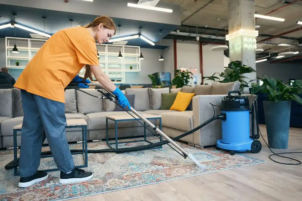 Bir kişi, oturma alanındaki halıyı endüstriyel elektrikli süpürgeyle temizliyor